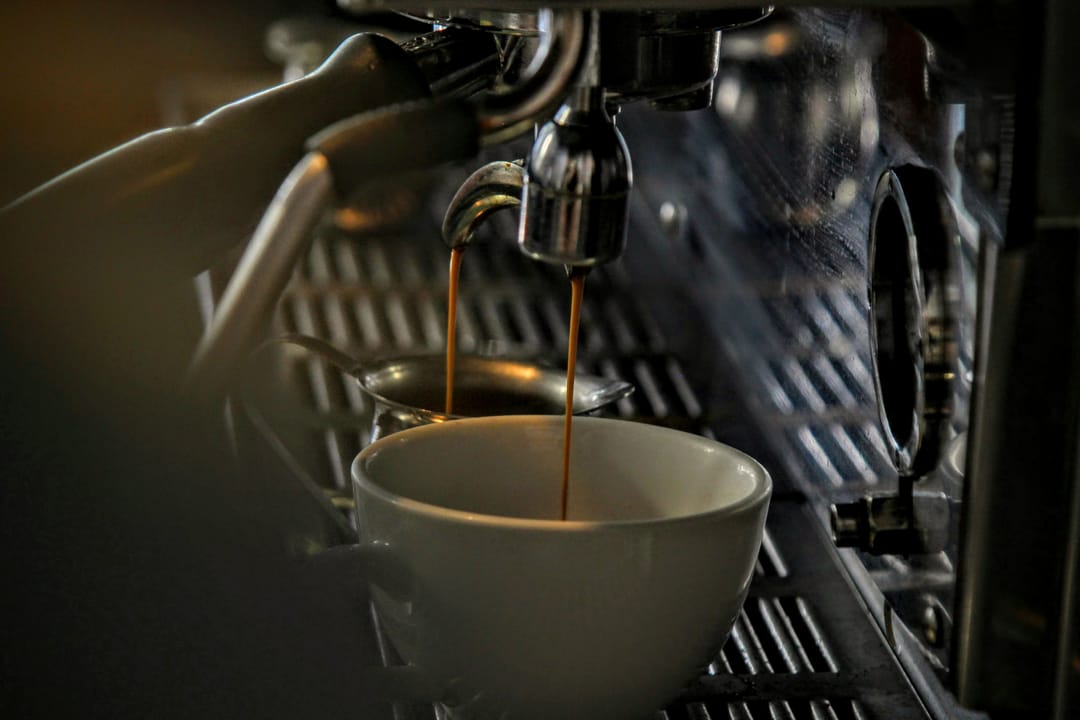 Espresso läuft in warmem Gegenlicht aus der Siebträgermaschine in eine weiße Tasse.